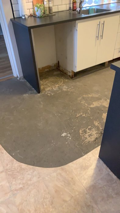 Kök med borttaget klickgolv och en skadad plastmatta som avslöjar den nakna betongen under diskbänken.