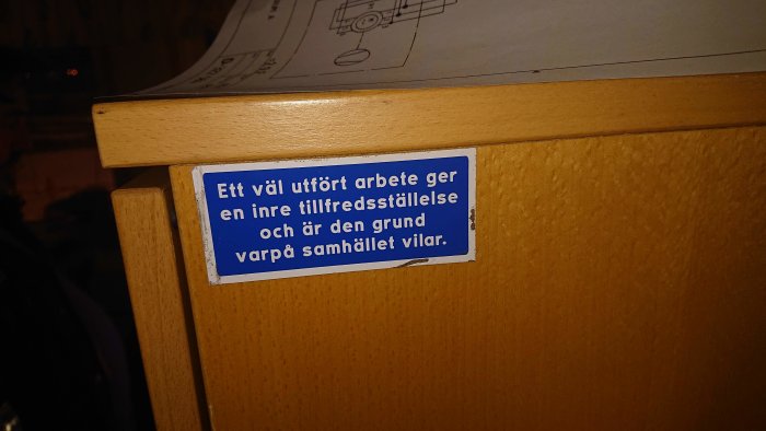 Dekal med texten "Ett väl utfört arbete ger en inre tillfredsställelse och är den grund varpå samhället vilar" på en byrålåda.