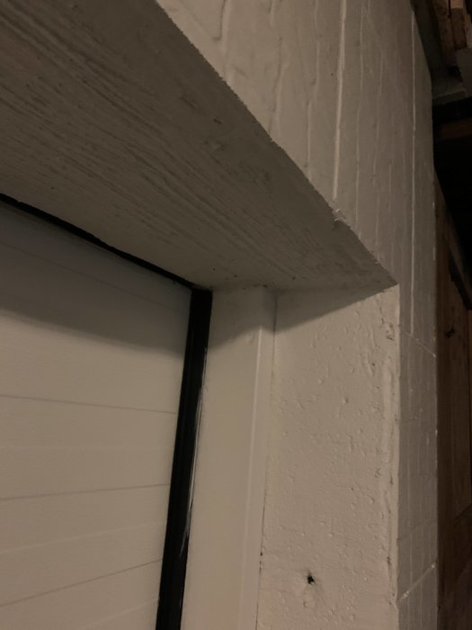 Hörnet av en vit garageport monterad i en betongvägg, potentiell plats för installation av 12V spottar.