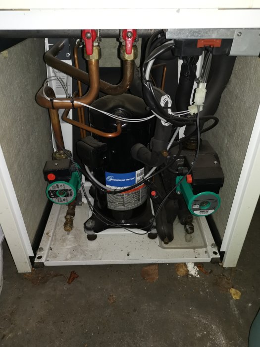 Installation av värmepump med kopparledningar, svart kondensor och två cirkulationspumpar.