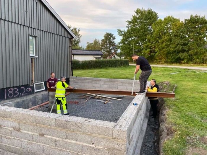 Tre personer arbetar på en grund med betongblock till en byggnad.