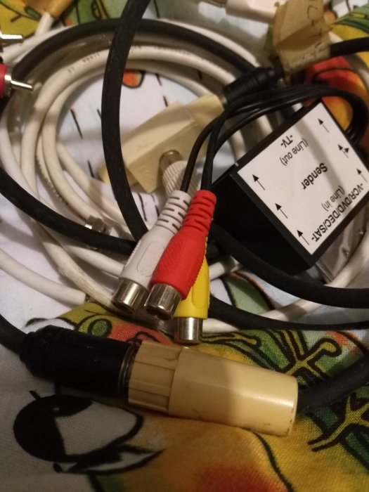 En samling gamla sladdar, inklusive RCA- och SCART-kablar, ovanpå en tygyta med mönster.