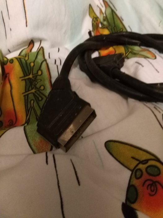 Scart-kontakt i änden av en svart kabel mot en bakgrund med färgglada mönster.