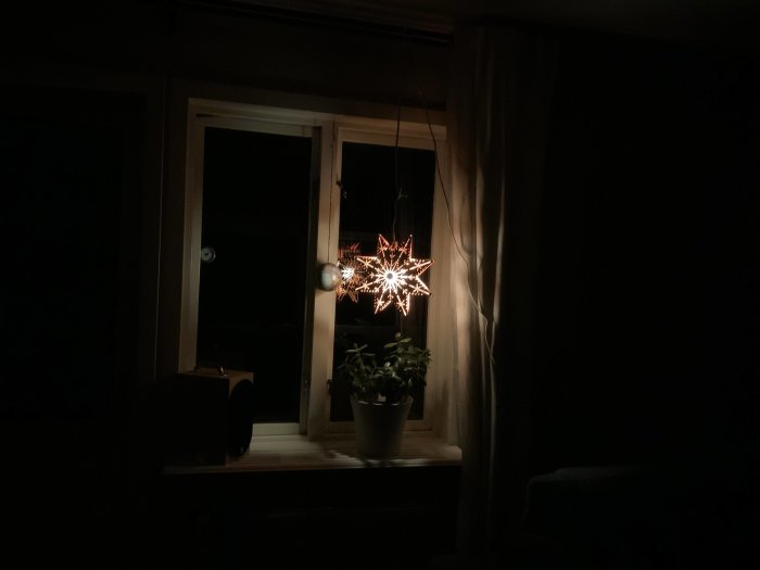 Julstjärna med vitbalanserad belysning från Philips HUE lampa i ett mörkt rum med fönster och gardiner.