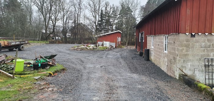 Nygrusad gårdsplan bredvid ladugård med byggmaterial och verktyg utspridda.