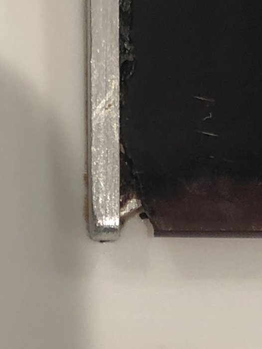 Närbild på skadat hörn av en svart induktionshäll med sargad kant.