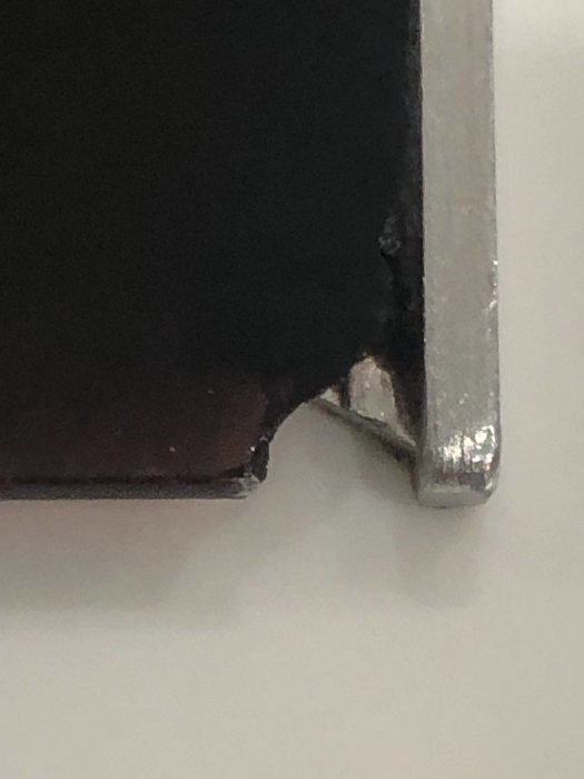 Närbild på hörnet av en induktionshäll med skador och avflagningar.