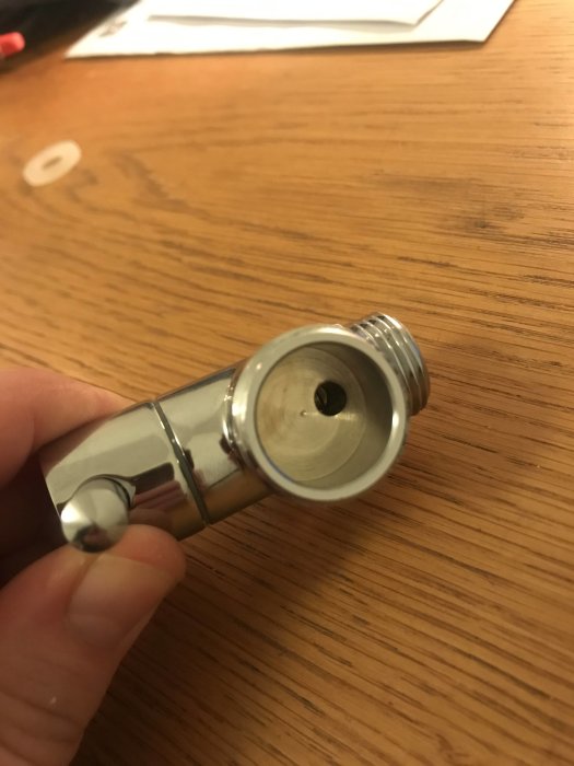 Omkastare för dusch med synlig gänga som hålls i en hand mot ett träbord.