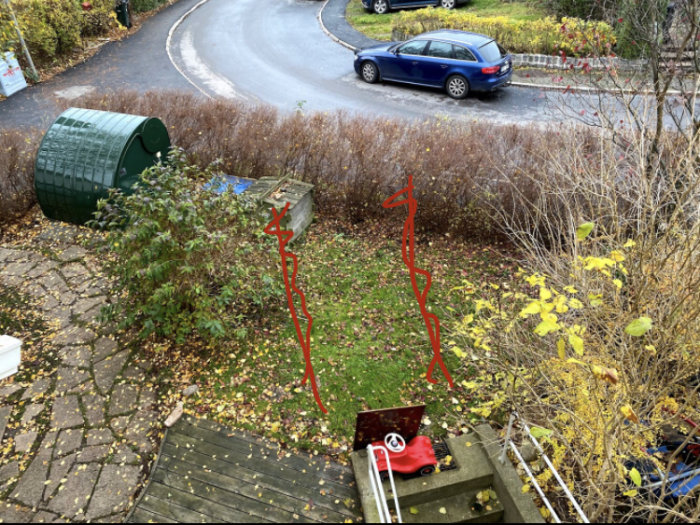 Vy över gräsmatta med rödmålade hjulspår där en tillfällig parkering är planerad, intill en bostad och en gata.