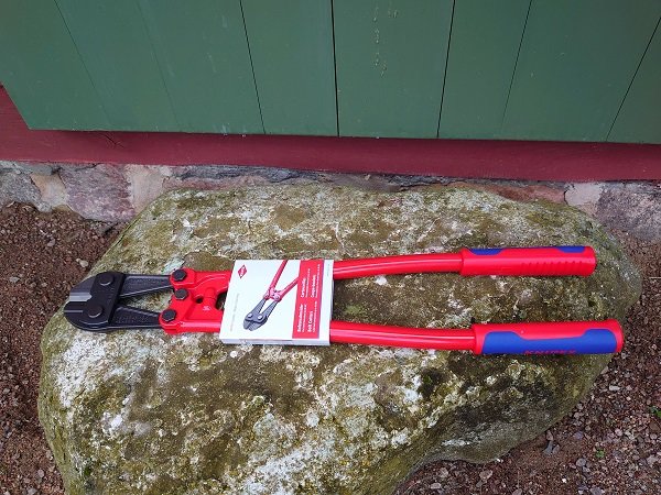 Ny Knipex-tång med rödblå handtag ligger på en sten framför en grön dörr.