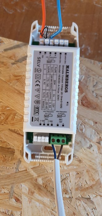 Elanslutning av en LED-driver från Malmbergs med anslutna kablar på en OSB-skiva i bakgrunden.