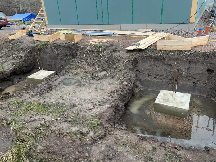 Grundarbete för carport med provisoriska upplag och gjutna fundament i marken.