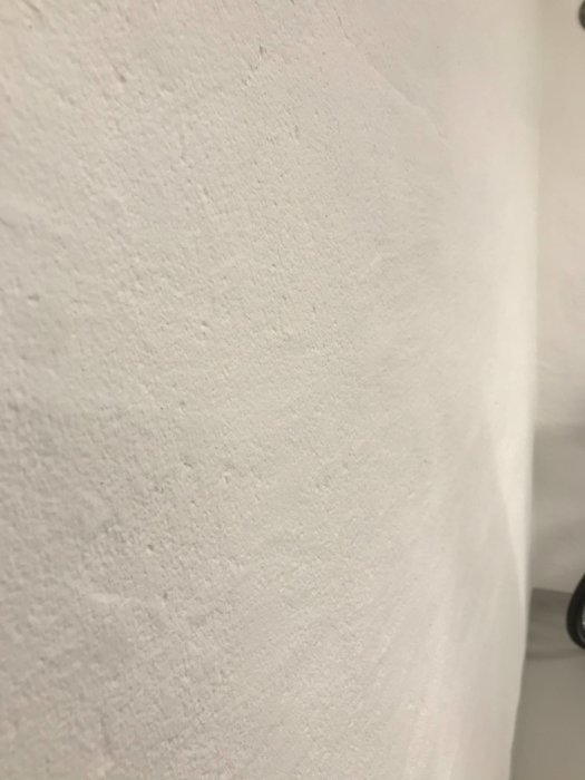 Närbild på en ojämn vitmålad vägg som visar resultatet av silikatfärg, med skuggning som ger djup.