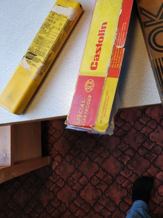 Svetsningselektroder från ESAB och Castolin i förpackningar på ett mönstrat golv.