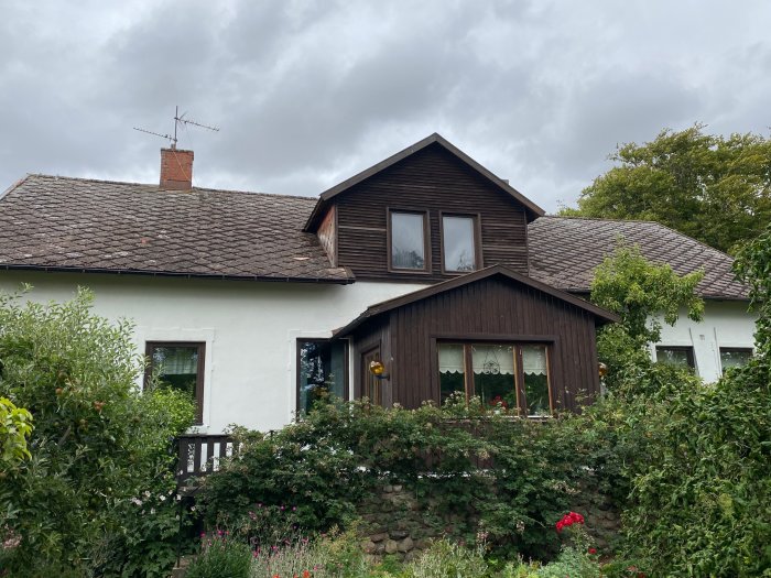 Hus med gammal veranda, vita putsväggar, mörkt tak och grönska, planer för ny öppning synlig.