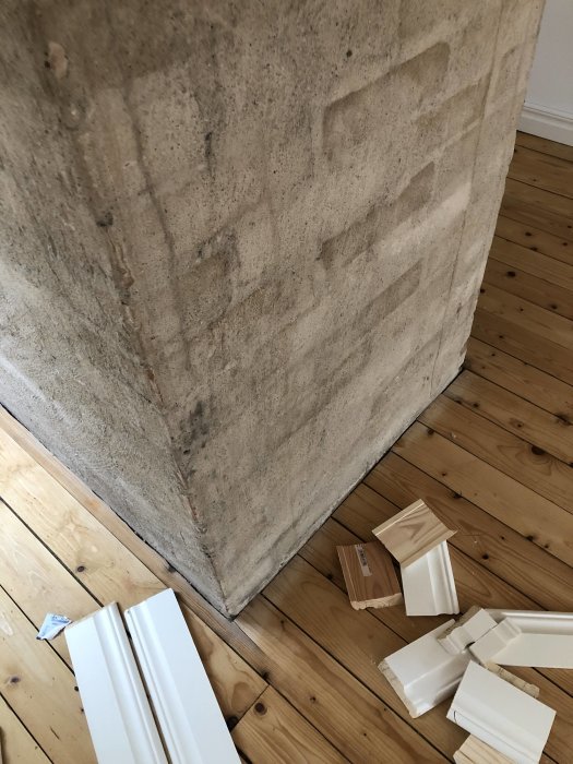 Vitlackerade lister på trägolv nära obehandlad murstock, fråga om dekorationslösning.