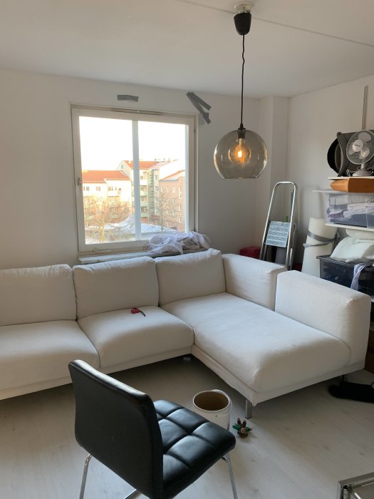 En rund glaslampa hänger från takdosa ovanför en vit hörnsoffa i ett ljust rum.