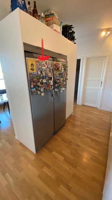 Kylskåp med dekaler och magneter, röd pil visar öppningsriktning från höger till vänster.