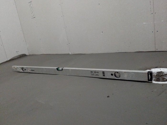 Nivåverktyg visar ojämnt flytspacklat golv med synlig svacka och oregelbundenhet.