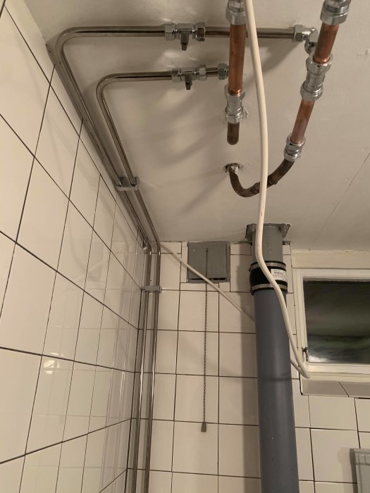 Nyinstallerade rör och avlopp i en renoverad källartoalett med vita kakelväggar.