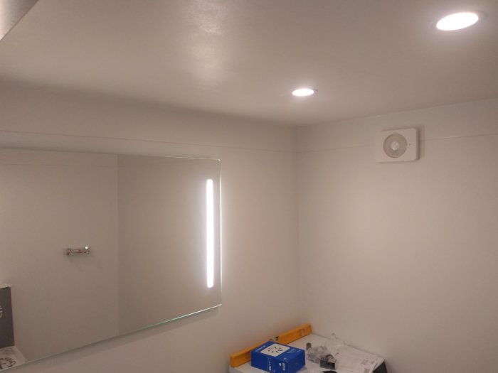 Renoverat badrum med LED-downlights i taket, belyst spegel, och Fresh fläkt, samt verktyg och material på golvet.