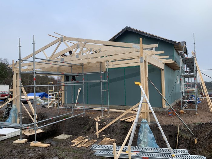 Konstruktion av träcarport med delvis uppfört tak, råspont och ströläkt under grått himmel.