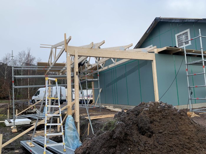 Konstruktion av trästomme för tak på carport vid hus, med byggmaterial och stegar runtom.