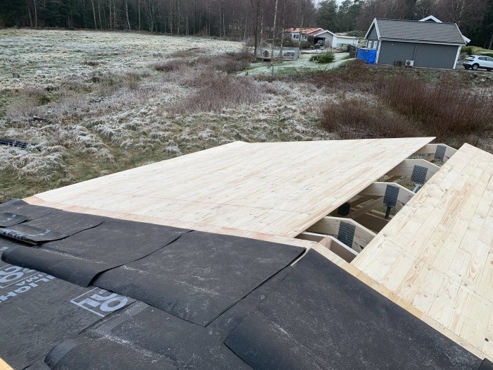 Takbyggnad med råspont och takpapp på en carport, delvis klar i frostigt landskap.