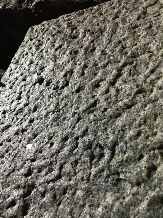 Närbild av grå granitsten med ojämn, porig yta som kan vara flammad eller krysshamrad.