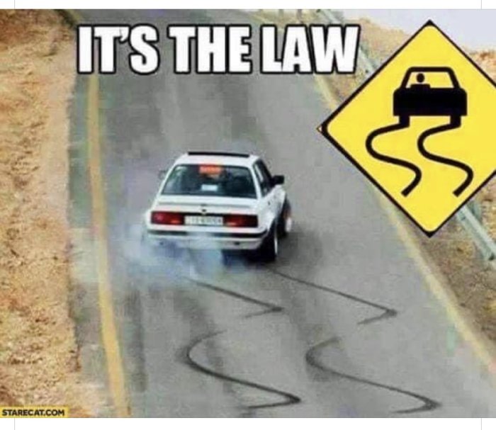 Bil som driftar på väg med rök bakom sig bredvid varningsskylt med glidande bil och text "IT'S THE LAW".