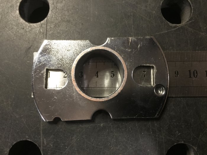 Metallplatta med hål och urklipp vid linjal, möjlig byggdel för att mäta eller fästa.