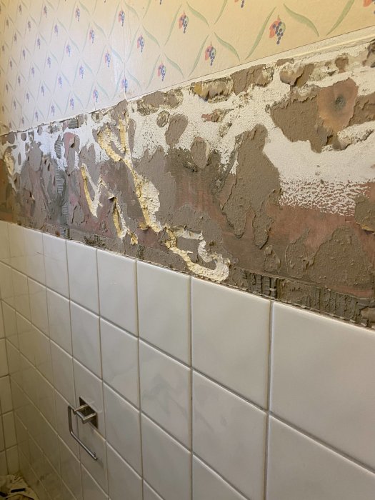 Vägg i badrum där kakel delvis är borttaget, exponerar bakomliggande murbruk och lim.
