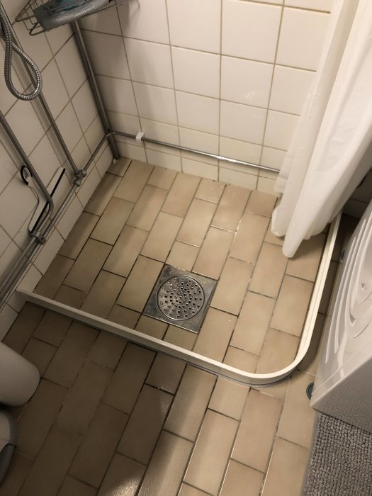 Badrumsbild som visar felaktigt fall på klinkergolv med vatten utanför duschområdet och slitna fogar.