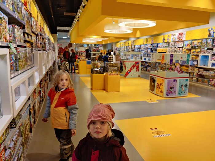 Två barn i en nästan tom leksaksbutik med hyllor fulla av leksaker och få kunder.