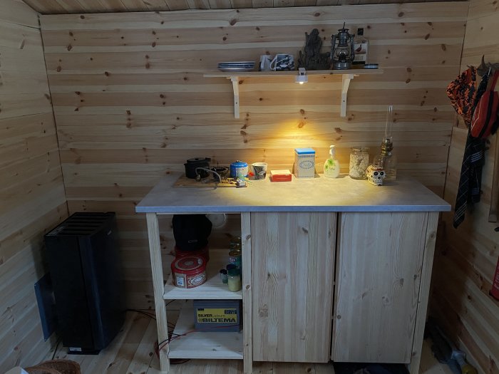 Köksmöbel byggd av IKEA-delar med bänkskiva ovanpå, i ett rum med träväggar och hylla med dekor.