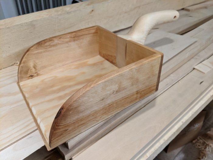 Handhållen träskyffel gjord av spillbitar ligger på en träbänk med träspån i verkstaden.