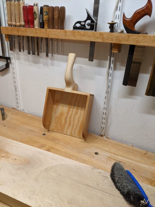 Handtillverkad träskyffel på arbetsbänk i en snickarverkstad, bredvid en kvast.