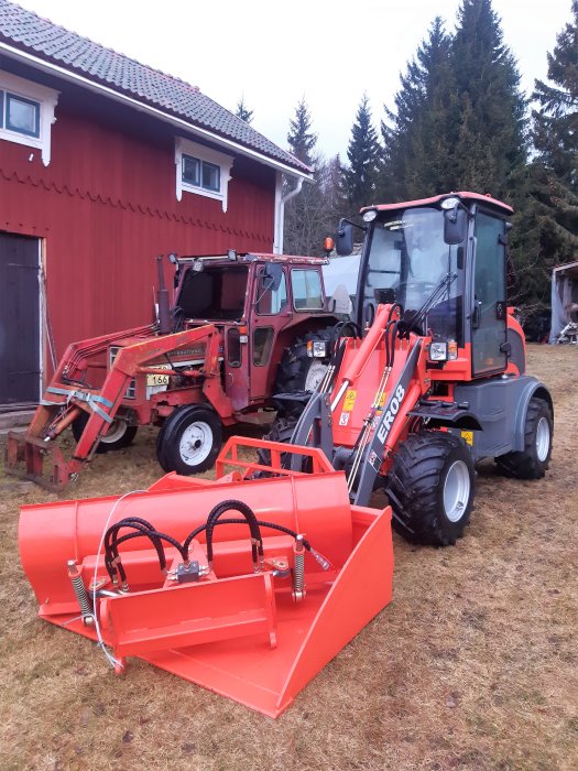 Röd traktor och en röd lastare framför ett rött hus, indikerar arbete på gården.