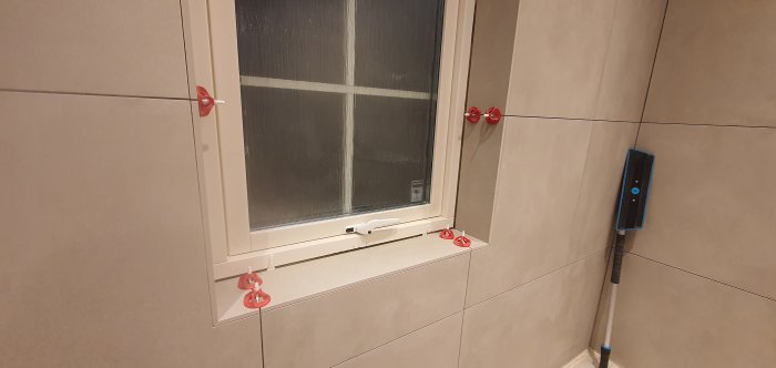 Nyinstallerat kakel runt fönster med polerade kanter och redskap för kakelsättning.