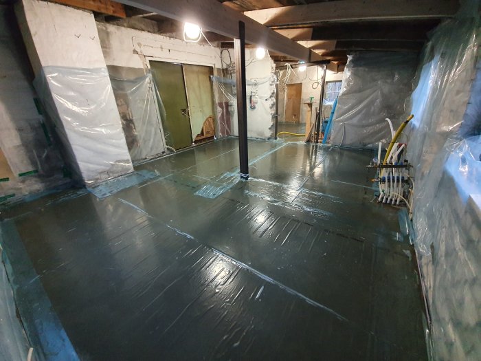 Oisolerat källarrum med nygjutet betonggolv och väggar täckta med plast.