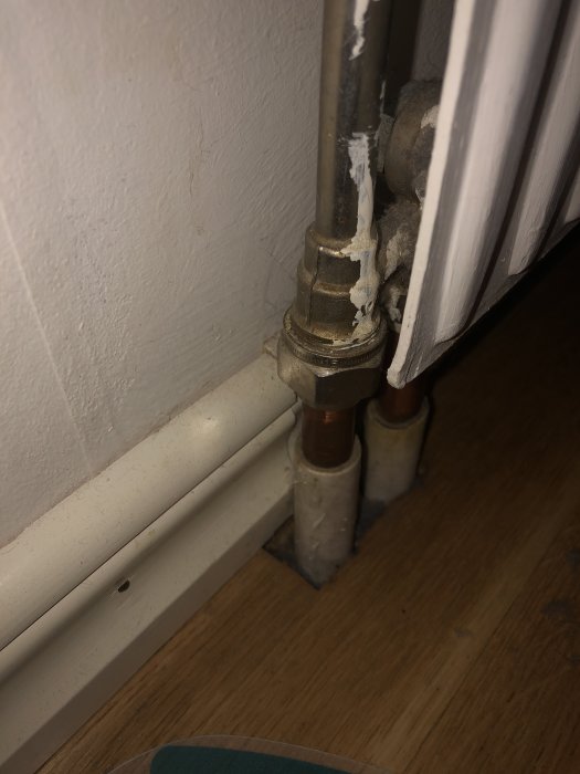 Kopplade kopparrör till en radiator som går genom golvet, med synliga anslutningsdetaljer.