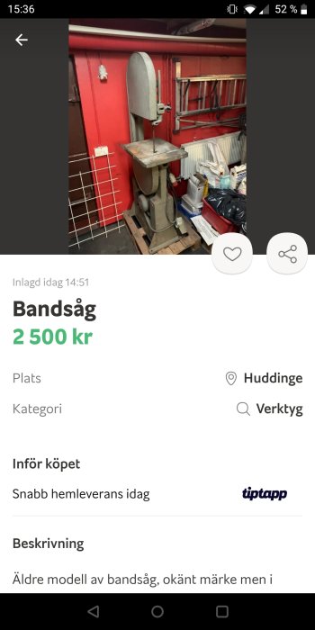 Äldre modell av vertikal bandsåg i en verkstad med röda väggar och diverse verktyg.