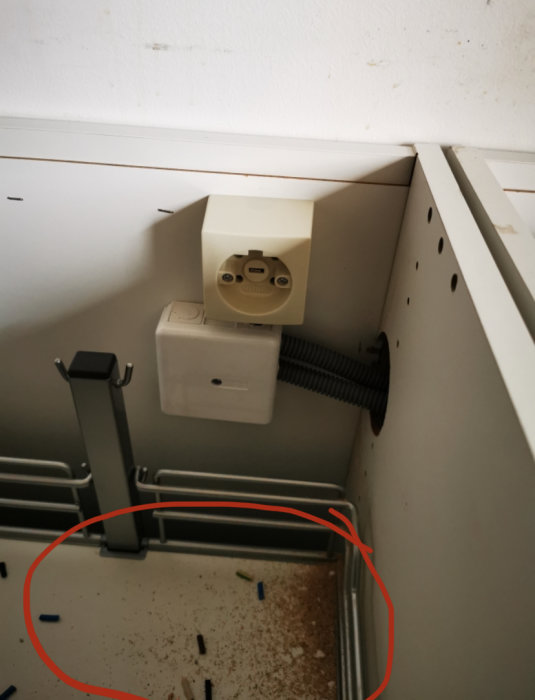 Oorganiserade elkablar och rester från installation i ett hörn med spår av borrning och klämmor på golvet.