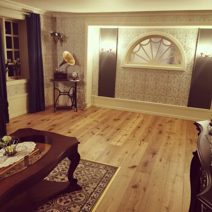 Ett nyligen renoverat tv-rum med mönstrade tapeter, trägolv, bord, mattor och en halvmåneformad överfönster.