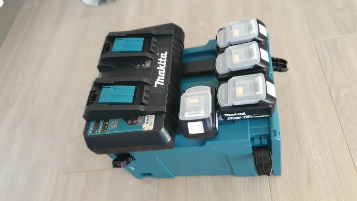 Makita-batteriladdare och fyra uppladdade batterier på ett golv, förberedda för användning.