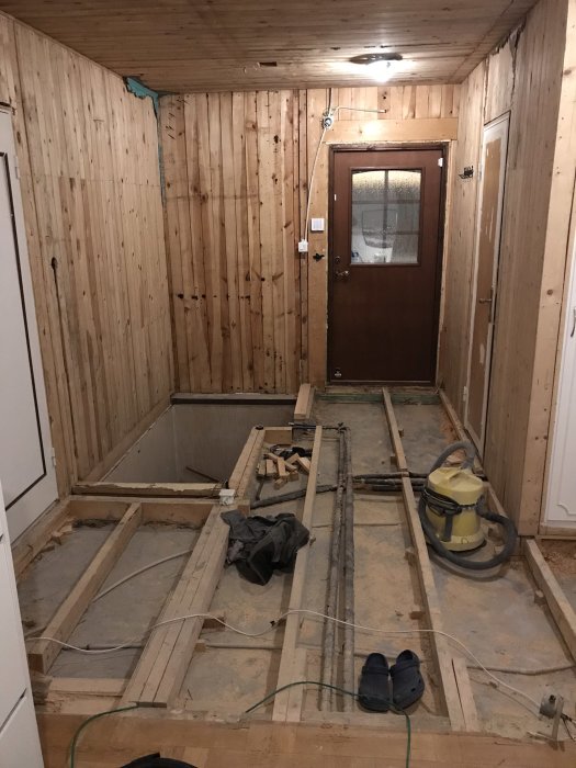 Renoveringsarbete med öppet golv för elinstallation och isolering, med träväggar och dörr.