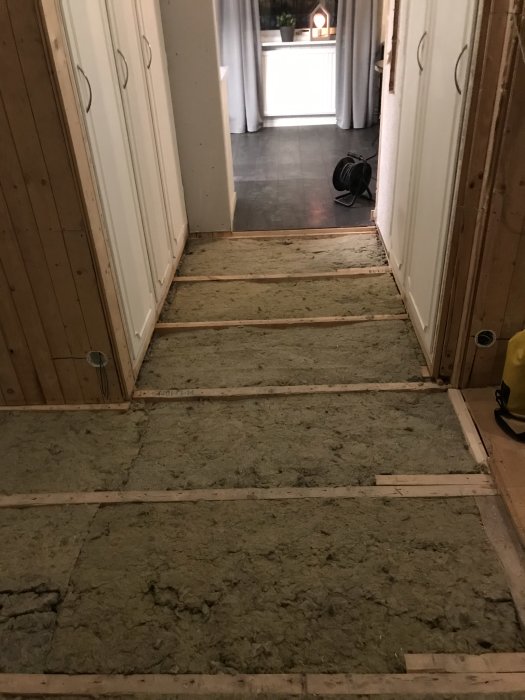 Gång i hus med ny isolering mellan träbjälkar och rörinstallationer synliga längs väggen.