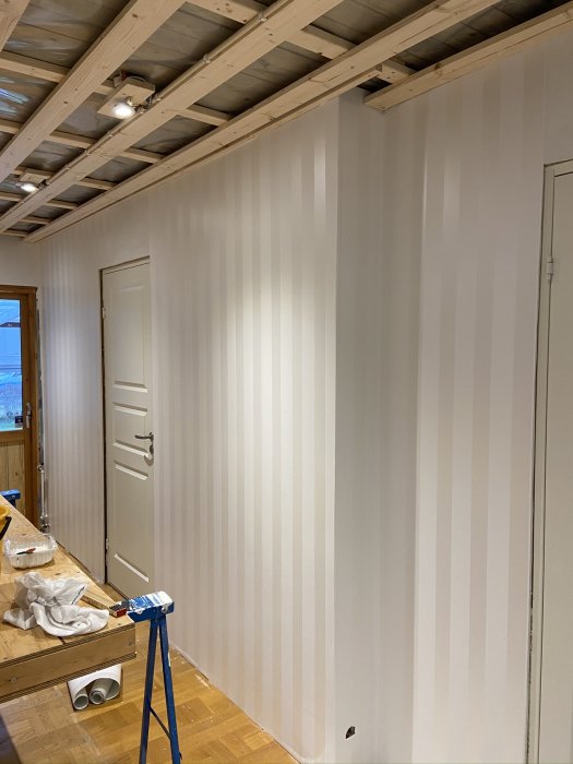 Renoverat rum med nytapetserade väggar i ljusa toner och ny innerdörr, byggmateriel synlig.