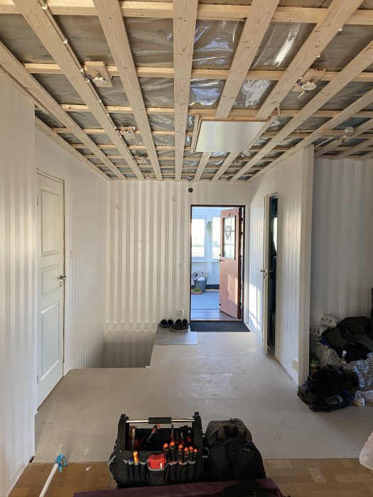 Rum under renovering med osatt tak, tapetserade och målade väggar samt nya vita innerdörrar.