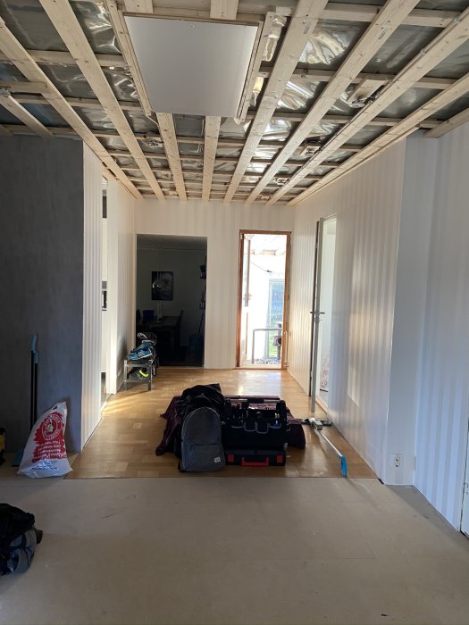 Renoveringsrum med öppet tak, väggar med ny tapet och omonterade innerdörrar, verktyg på golvet.